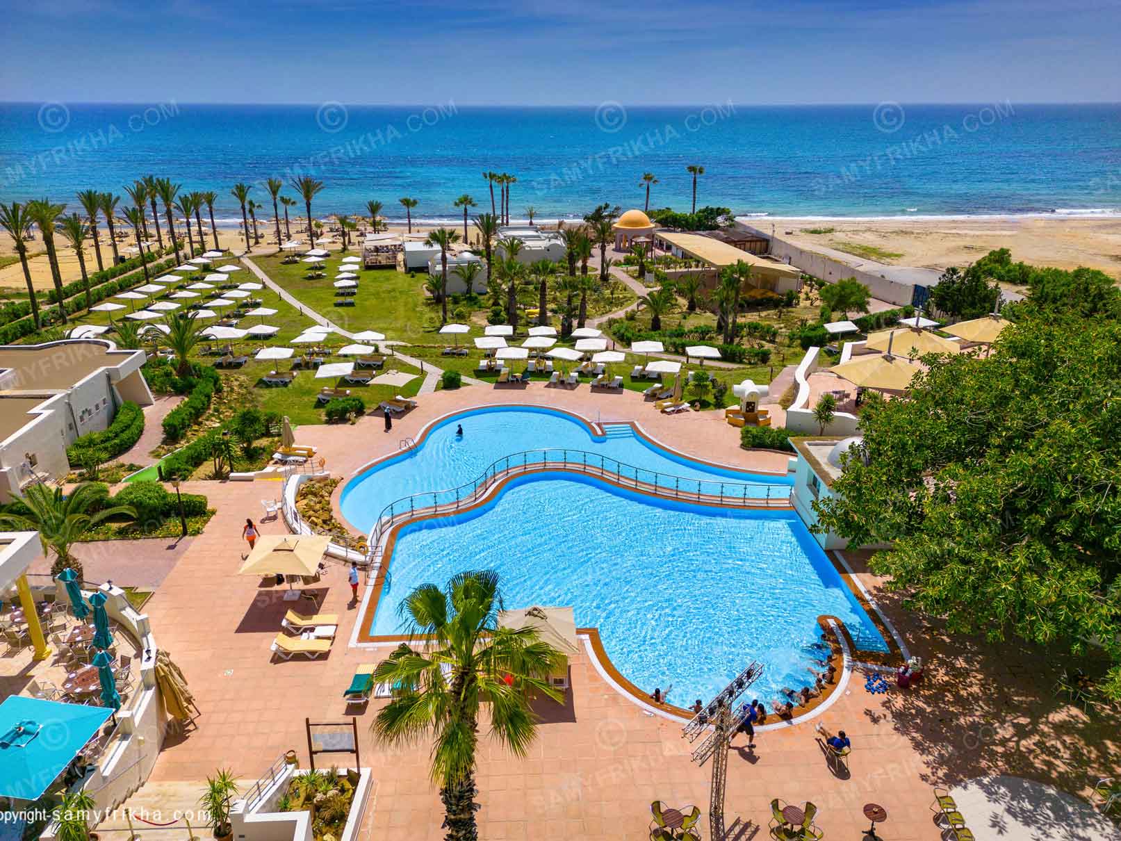 Piscine d'hôtel et plage aménagée photographiées depuis les airs.