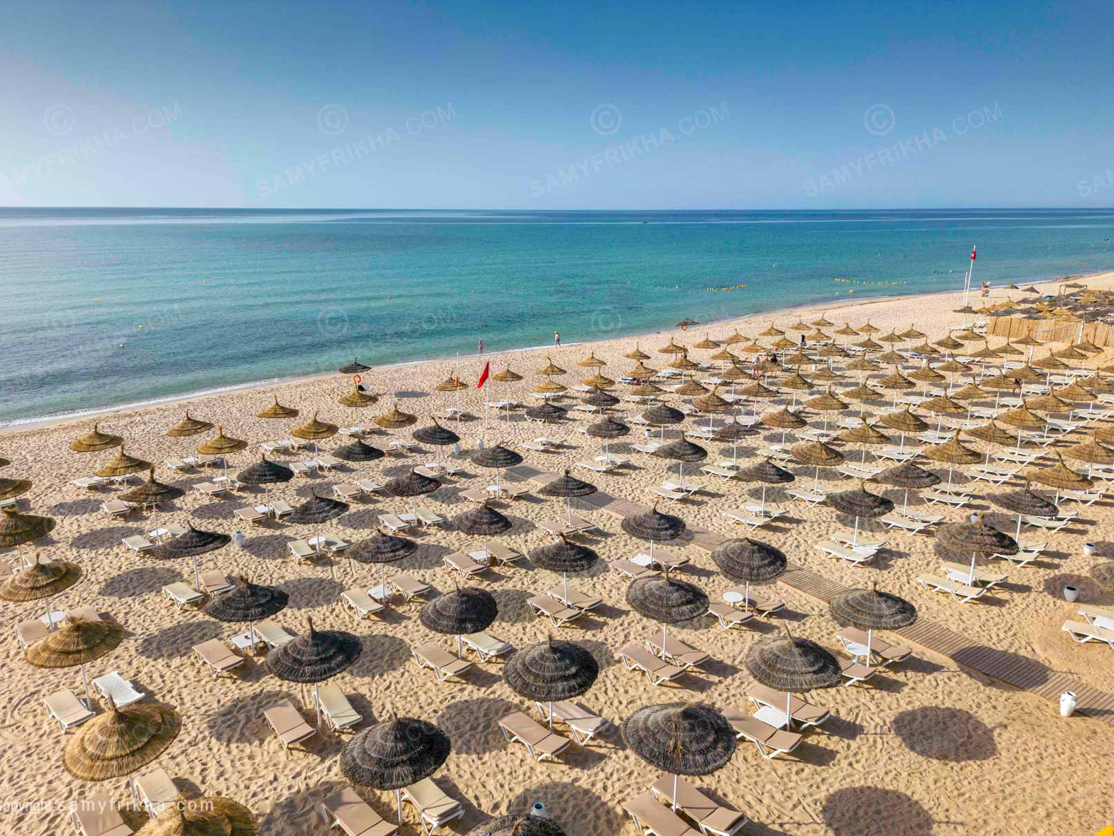 Vue aérienne d'une plage d'hôtel avec de nombreux parasols au bord de la mer.