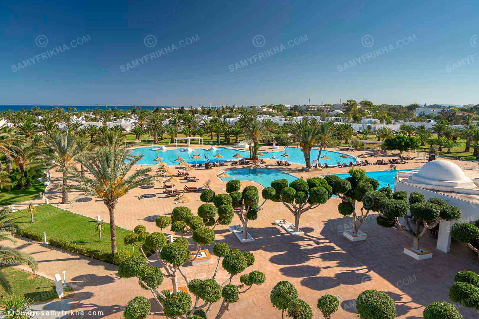 Vue aérienne d'un hôtel avec piscine, jardins et plage en bord de mer
