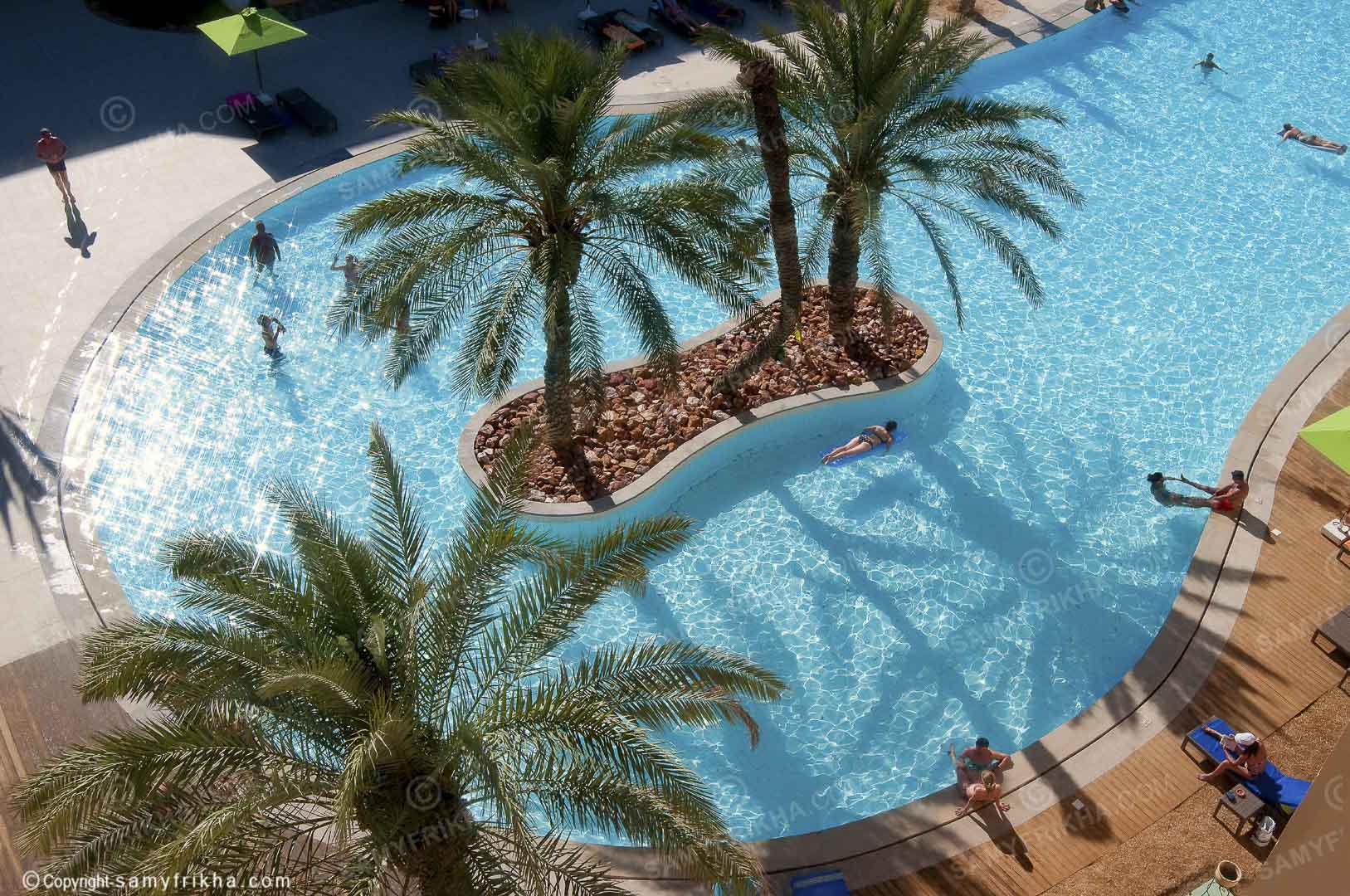 Piscine d'hôtel entourée de palmiers photographiée depuis les airs.